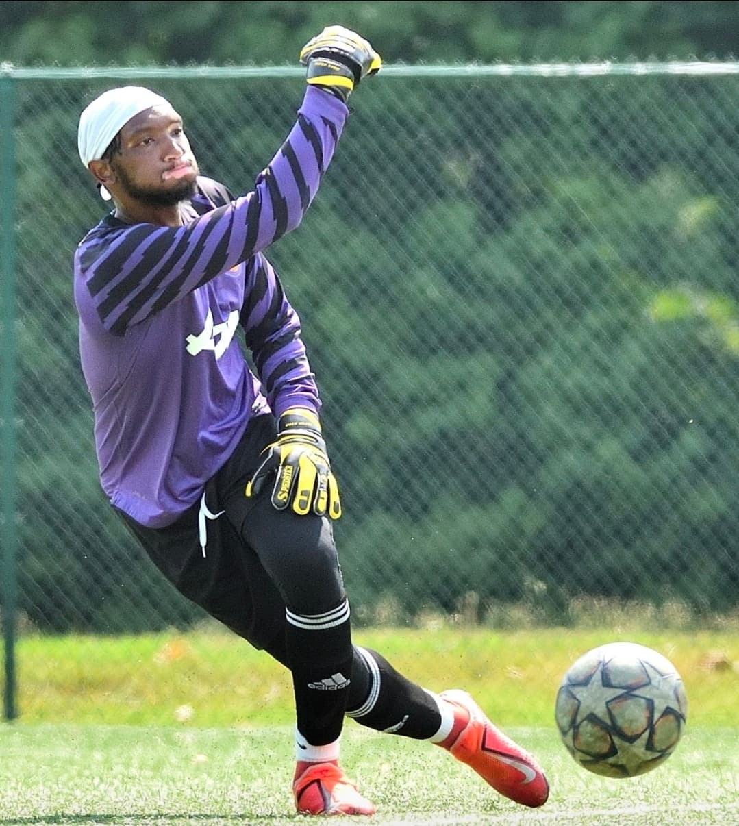 A JFC goalkeeper in purple kit sending the ball away