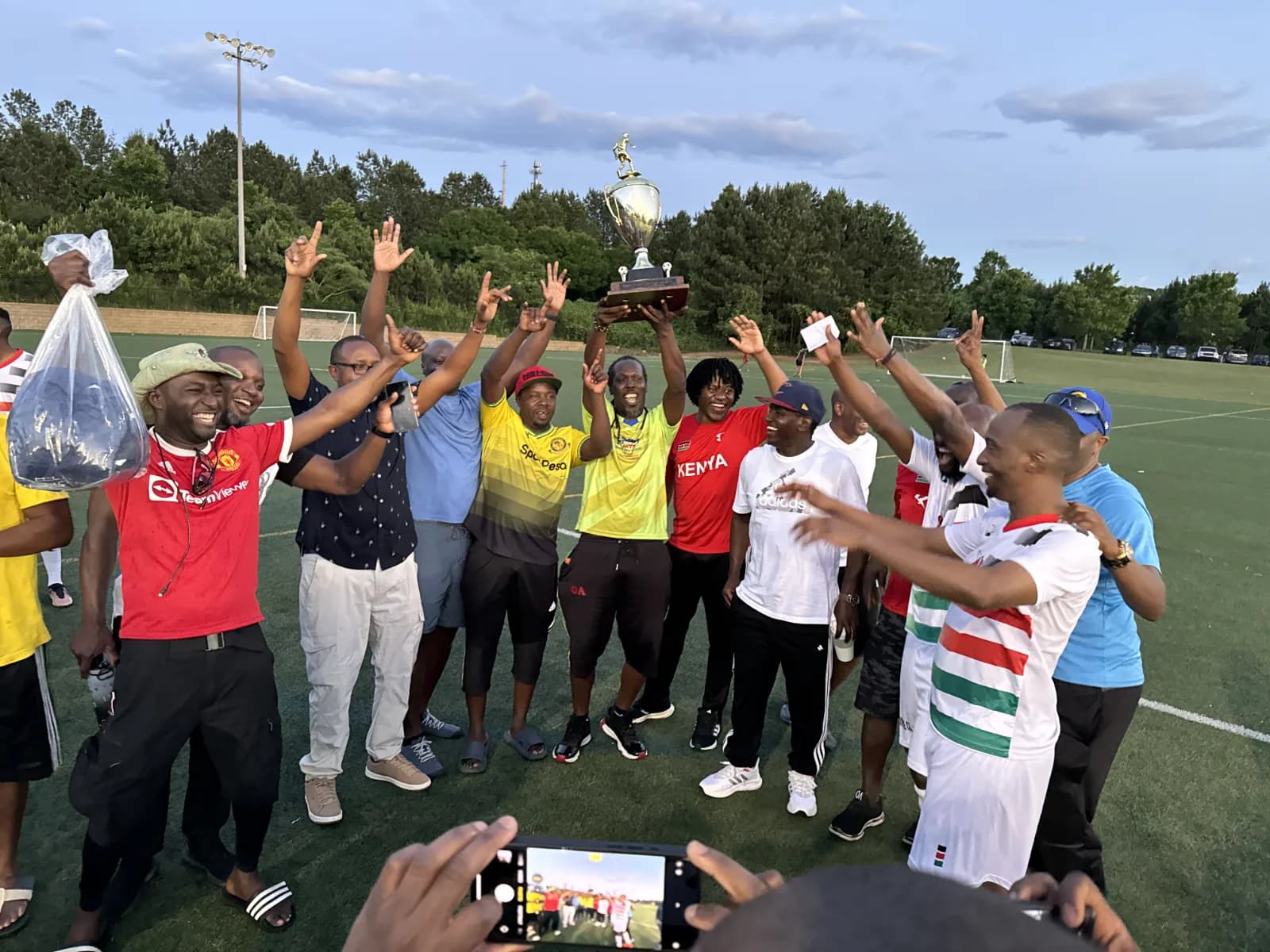 Players and supporters cheering with arms raised around the trophy