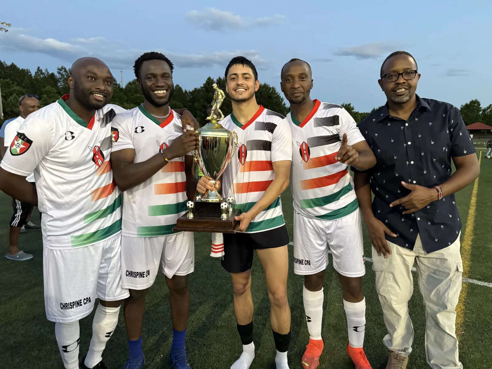 Five men in club kit and a shirt-sleeved supporter holding the trophy together