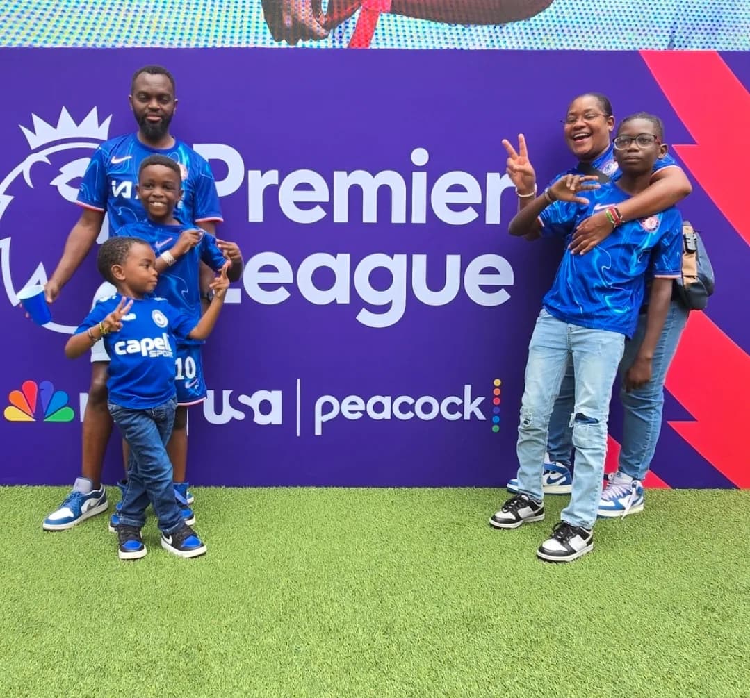 Two adults and two boys in blue football shirts posing in front of a Premier League backdrop