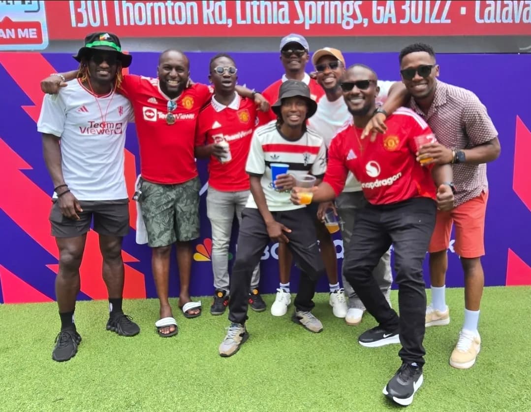 A group of friends in red and white football shirts posing together in front of a sponsor wall