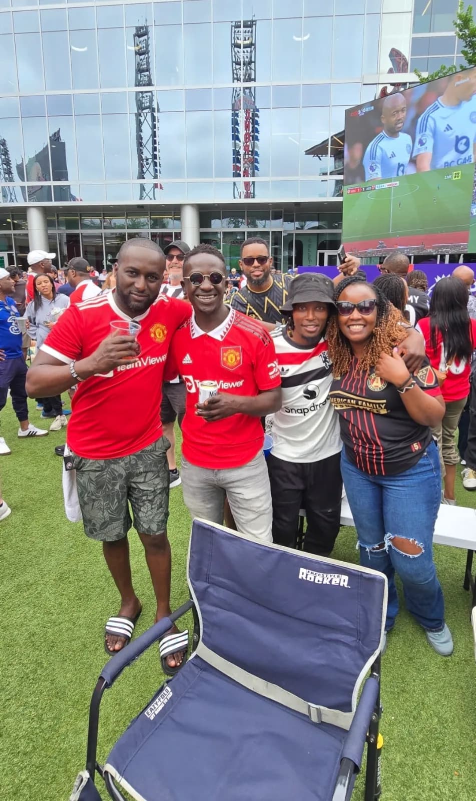 Friends in red football shirts posing on the grass with the big screen behind them