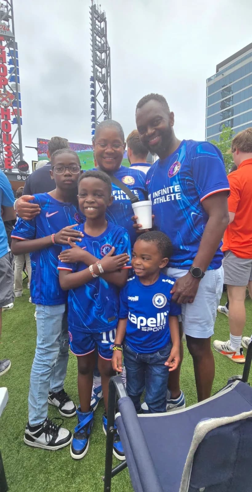 A man and three boys in blue kits standing together on the grass at the watch party