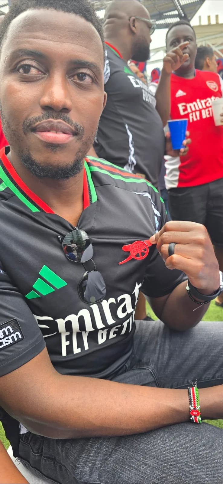A supporter in a black Arsenal shirt sitting in the crowd, red shirts all around