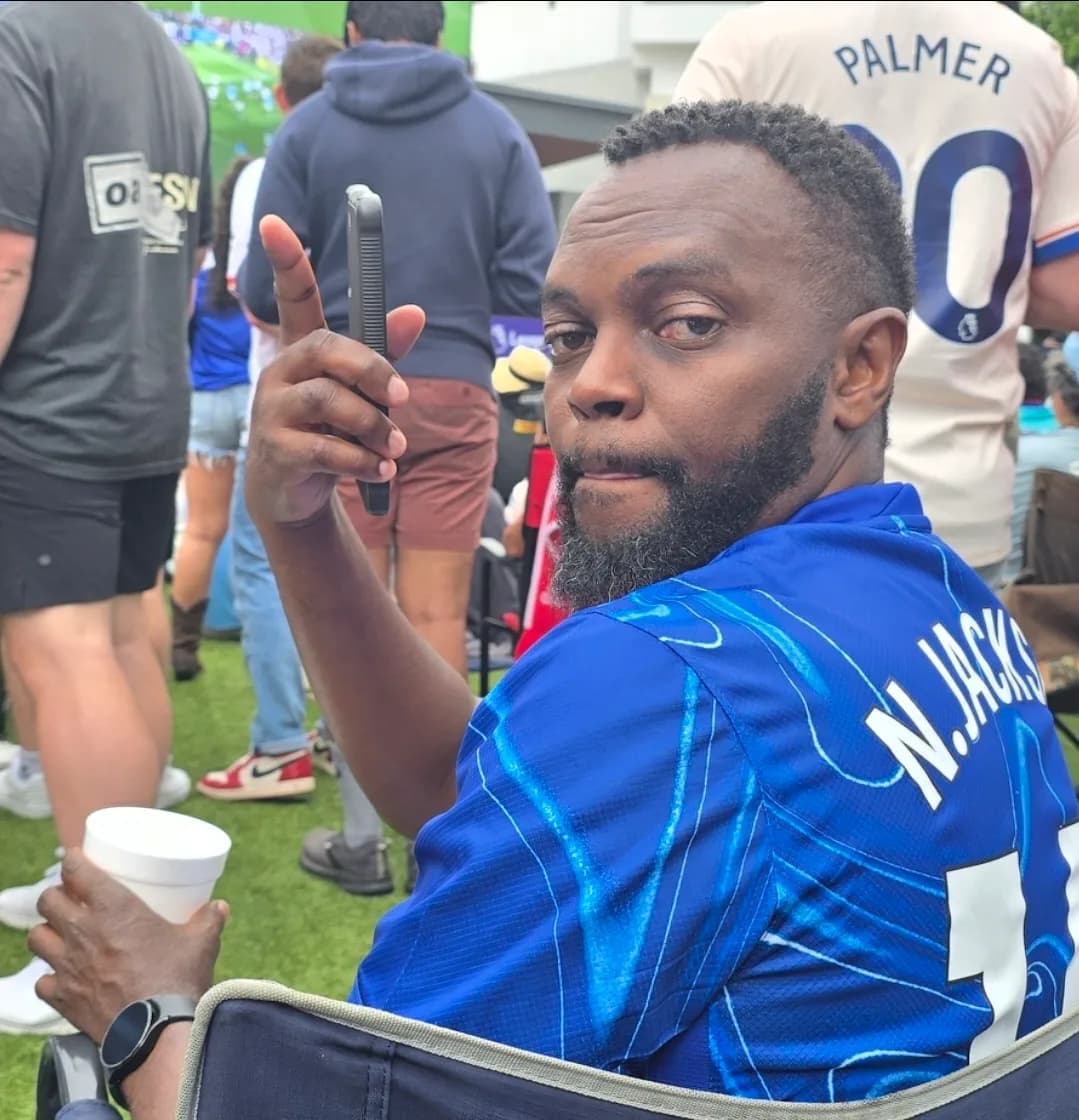 A supporter in a blue Chelsea shirt pointing up at the camera from his chair