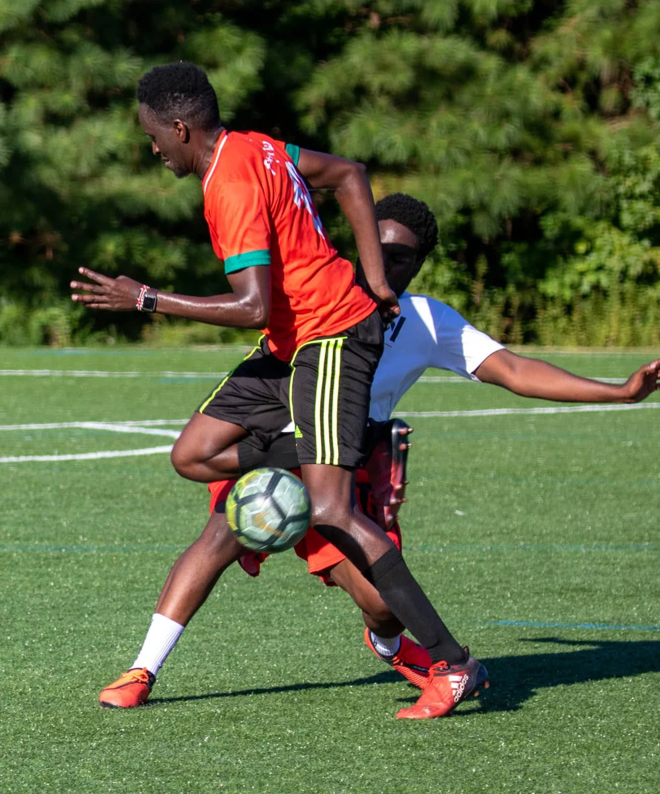 Two players tangle for the ball in a tackle on a sunny pitch