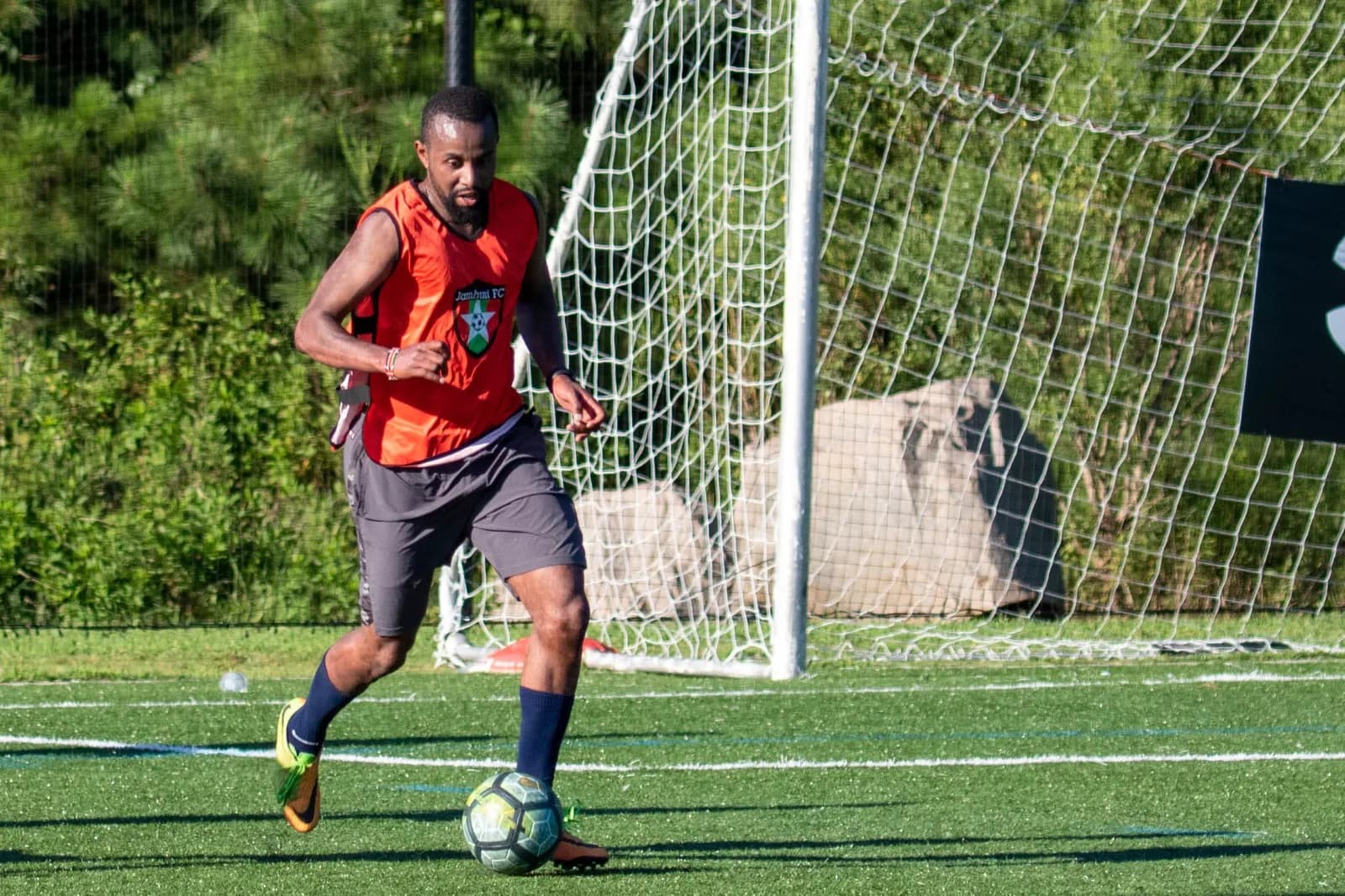 A player in an orange bib dribbling past the goal