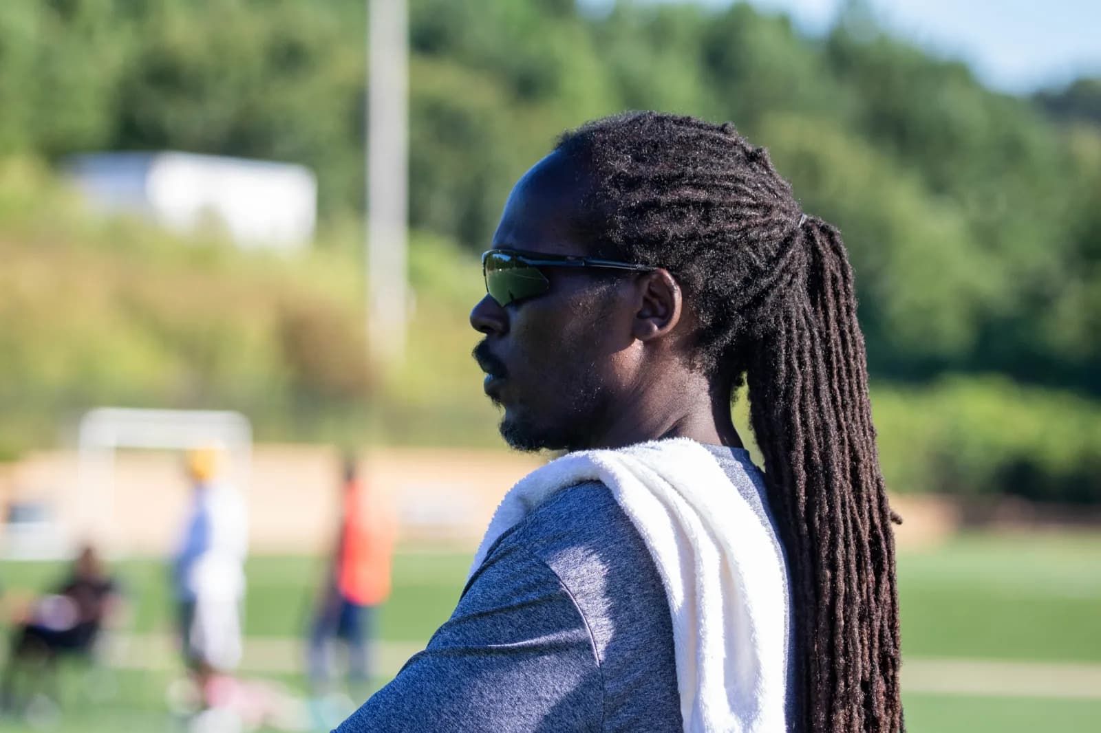 A man with locs and sunglasses watching from the touchline