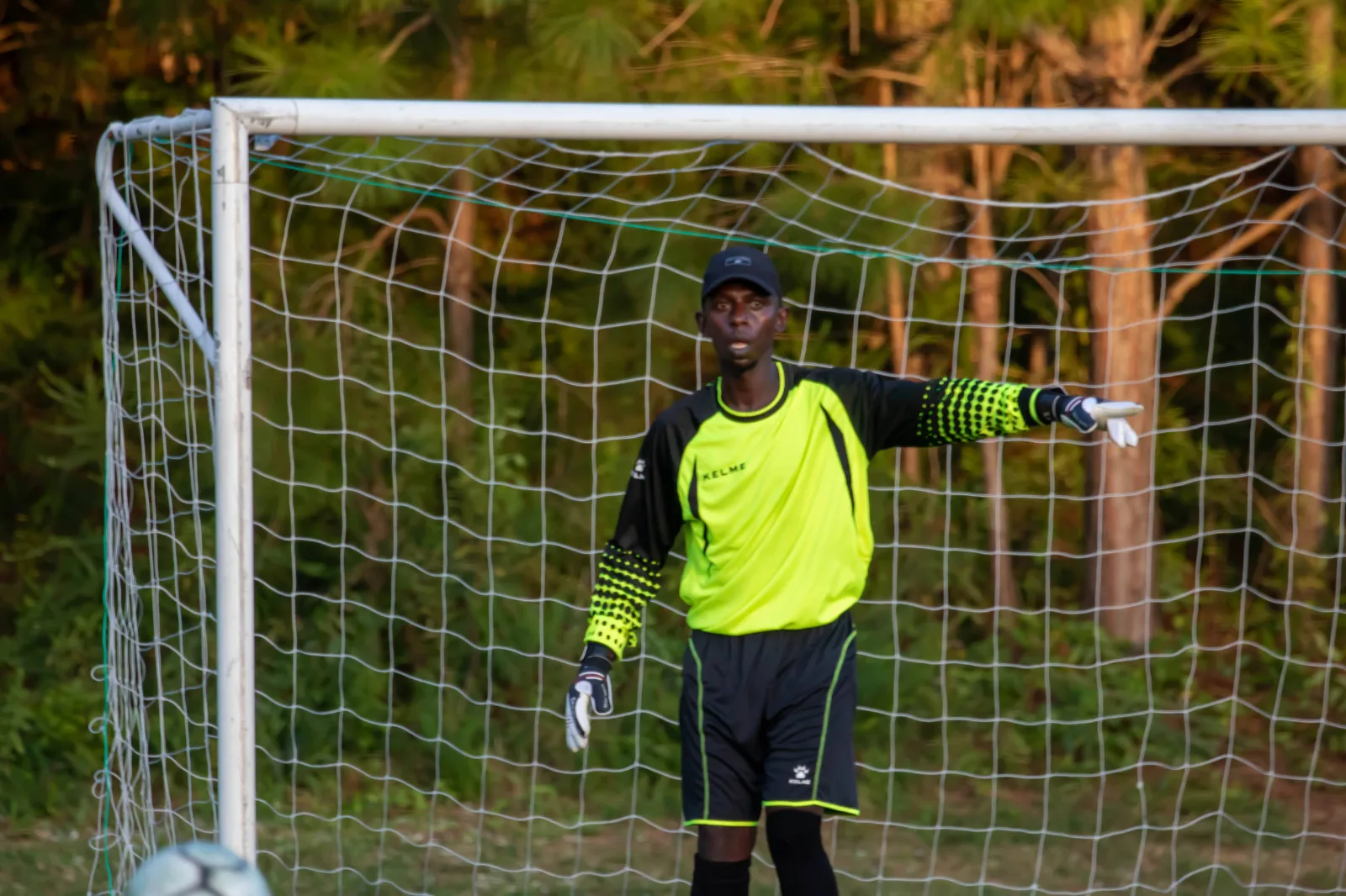 A goalkeeper in a yellow top pointing instructions to his defence