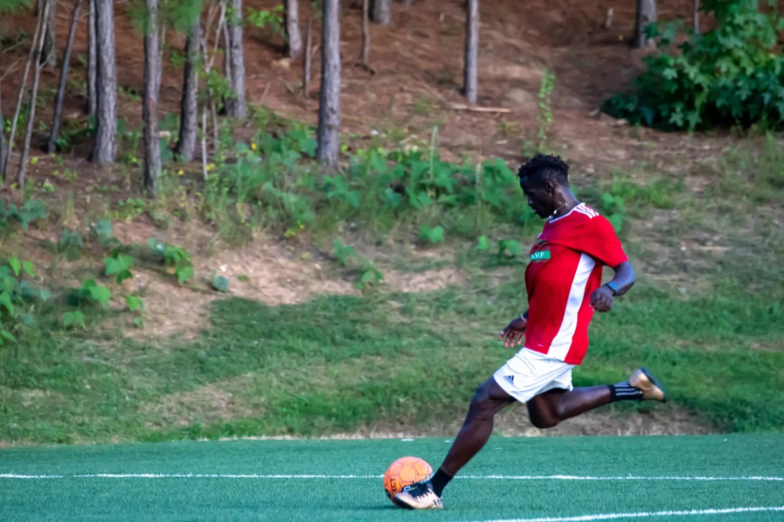A player in red striking the ball from the edge of the grass