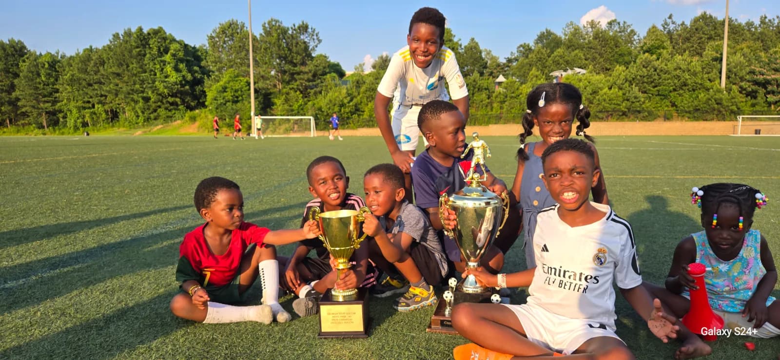 Children sitting on the grass around the trophies, smiling