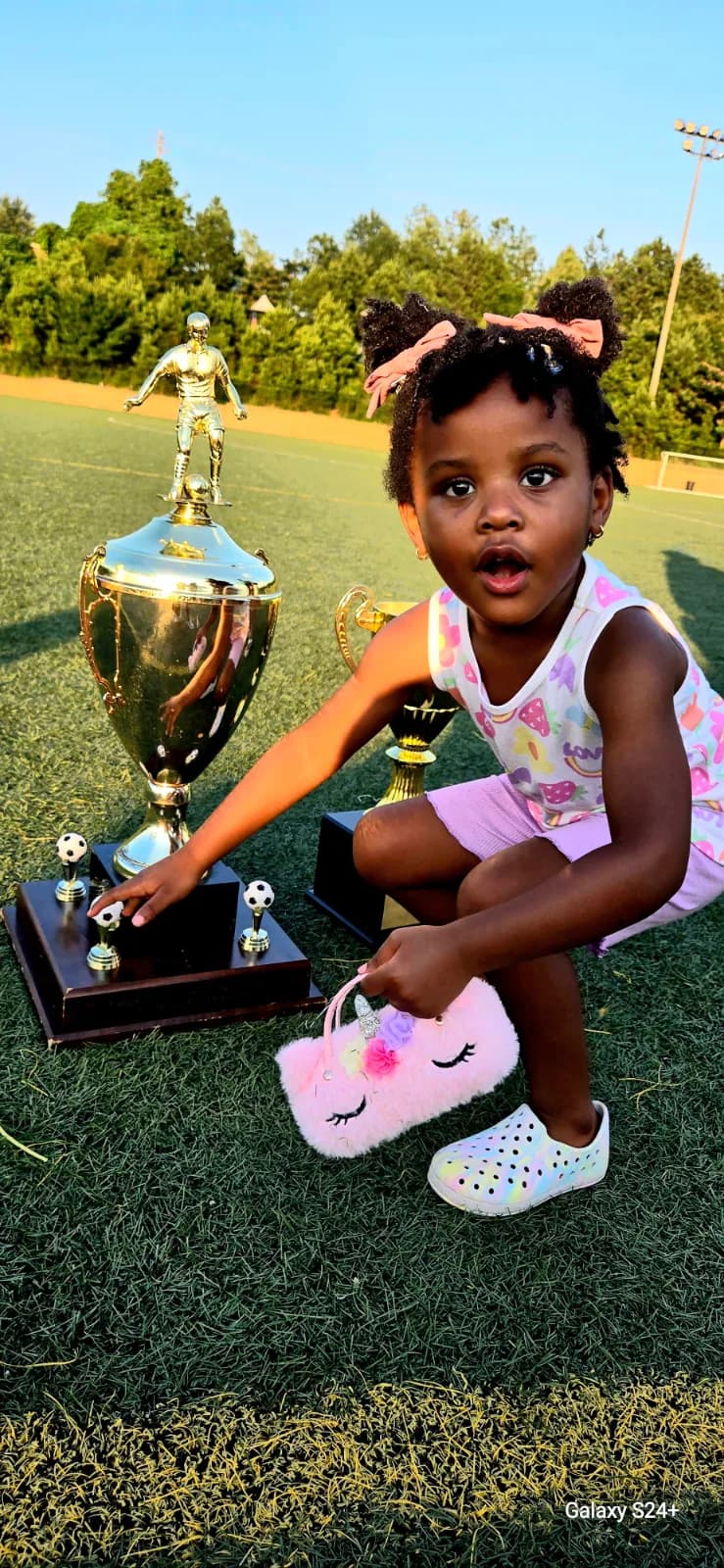 A small girl crouching beside the big gold trophy