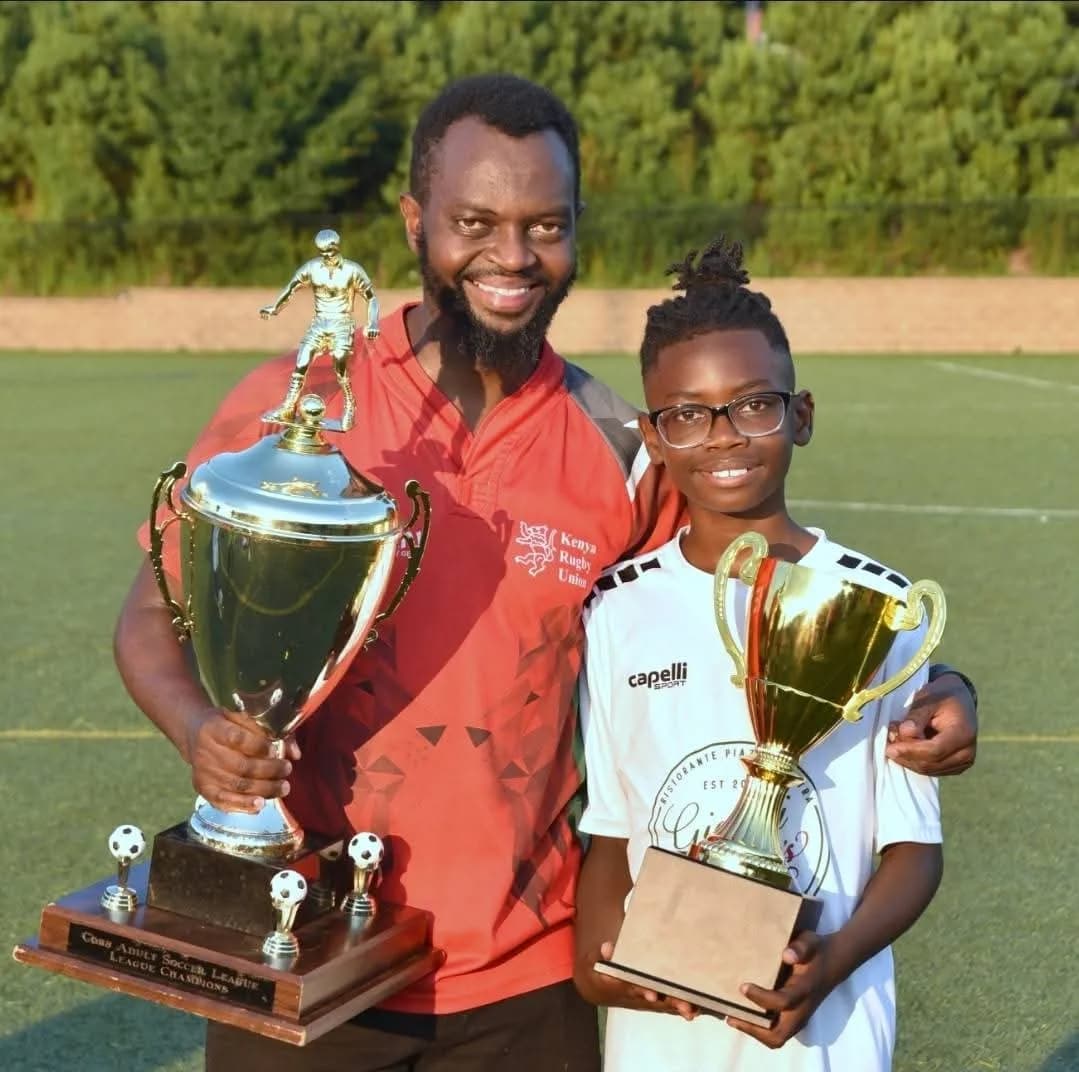 A man and a young player in glasses each holding a trophy, both smiling