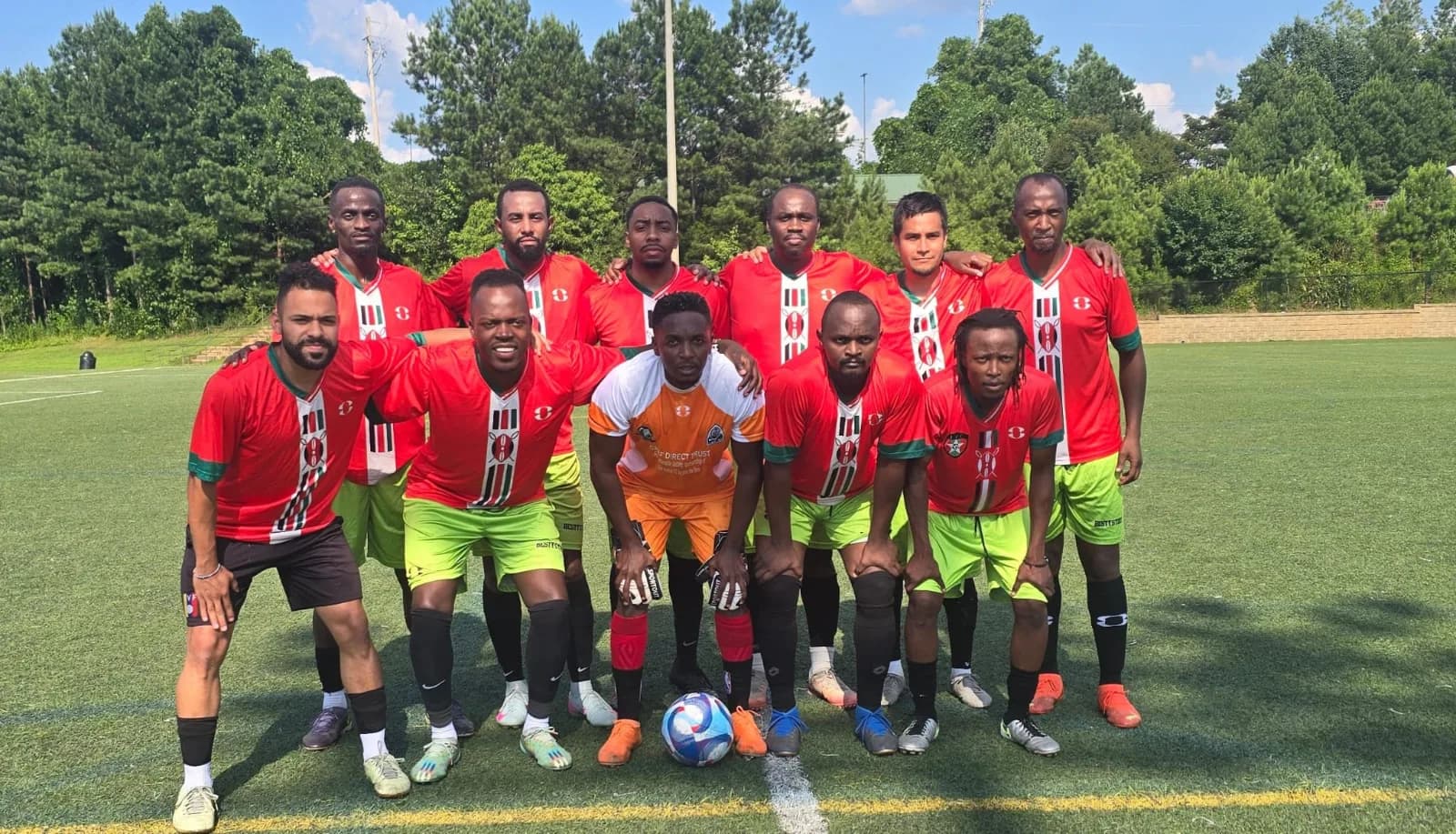 A squad in red and lime kit lined up for a team photo on a sunny pitch