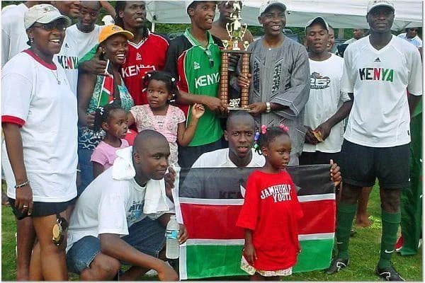 Early JFC players and families around a trophy and a Kenyan flag