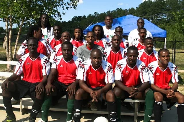 JFC players in red shirts seated on a bench in front of the team tent