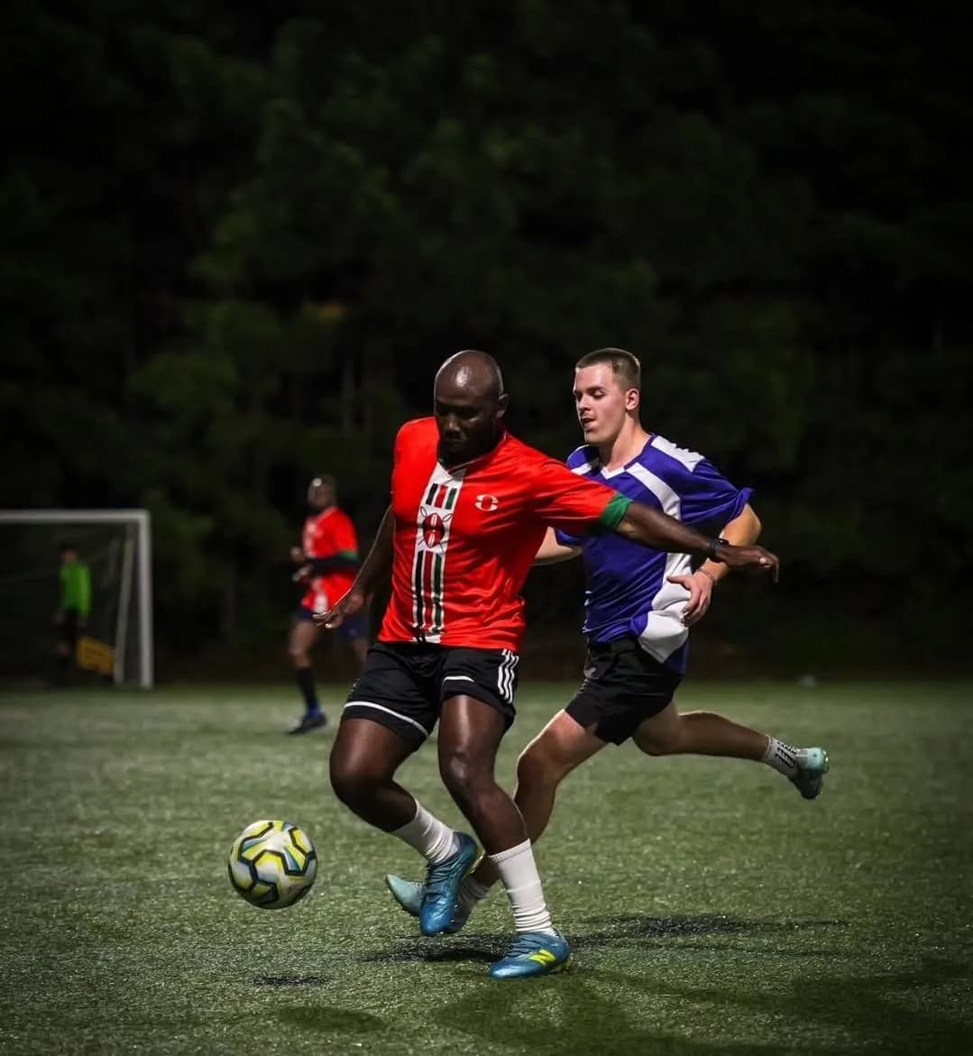 A JFC player in red holding off a defender in purple as they chase the ball at night
