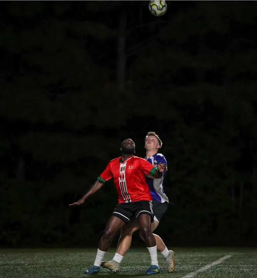 A JFC player in red shielding a defender as the ball drops out of the night sky