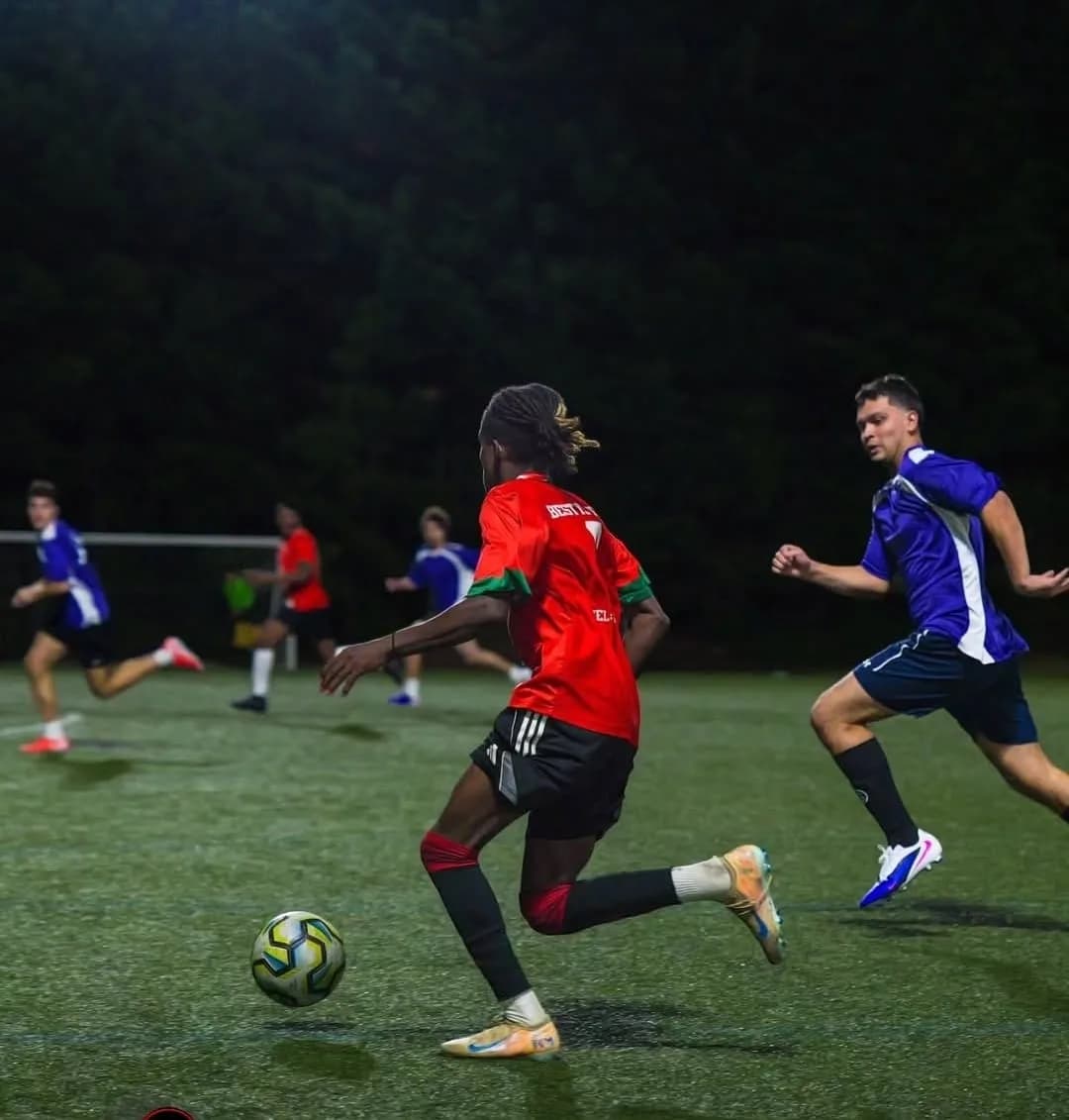 A JFC player in red running onto the ball with a defender in purple chasing