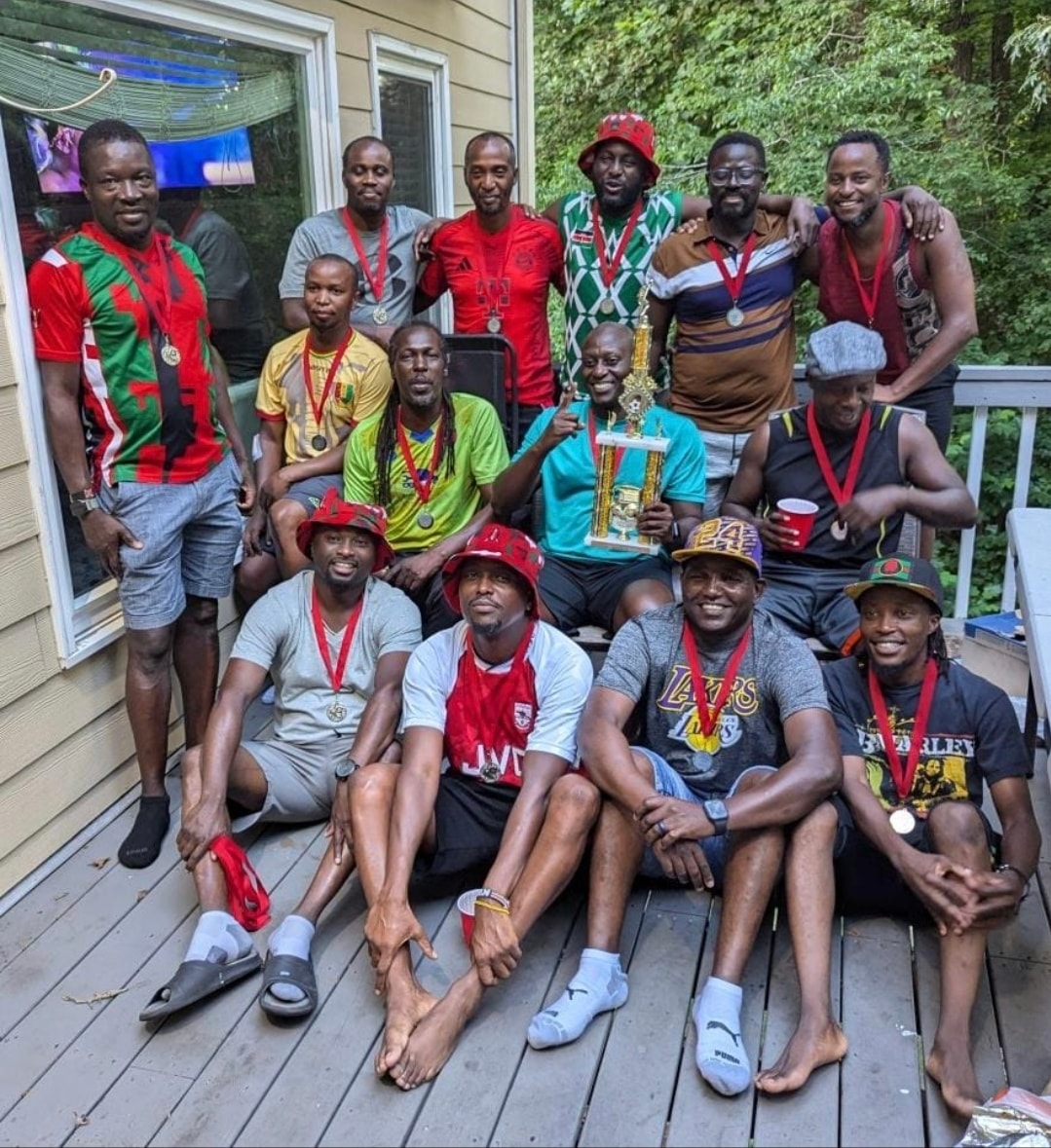 JFC players and friends gathered on a deck with a trophy, all wearing medals