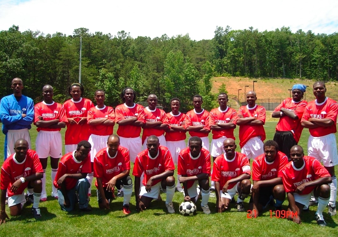 An early Jamhuri FC team in red kit, standing and kneeling in two rows on a grass pitch