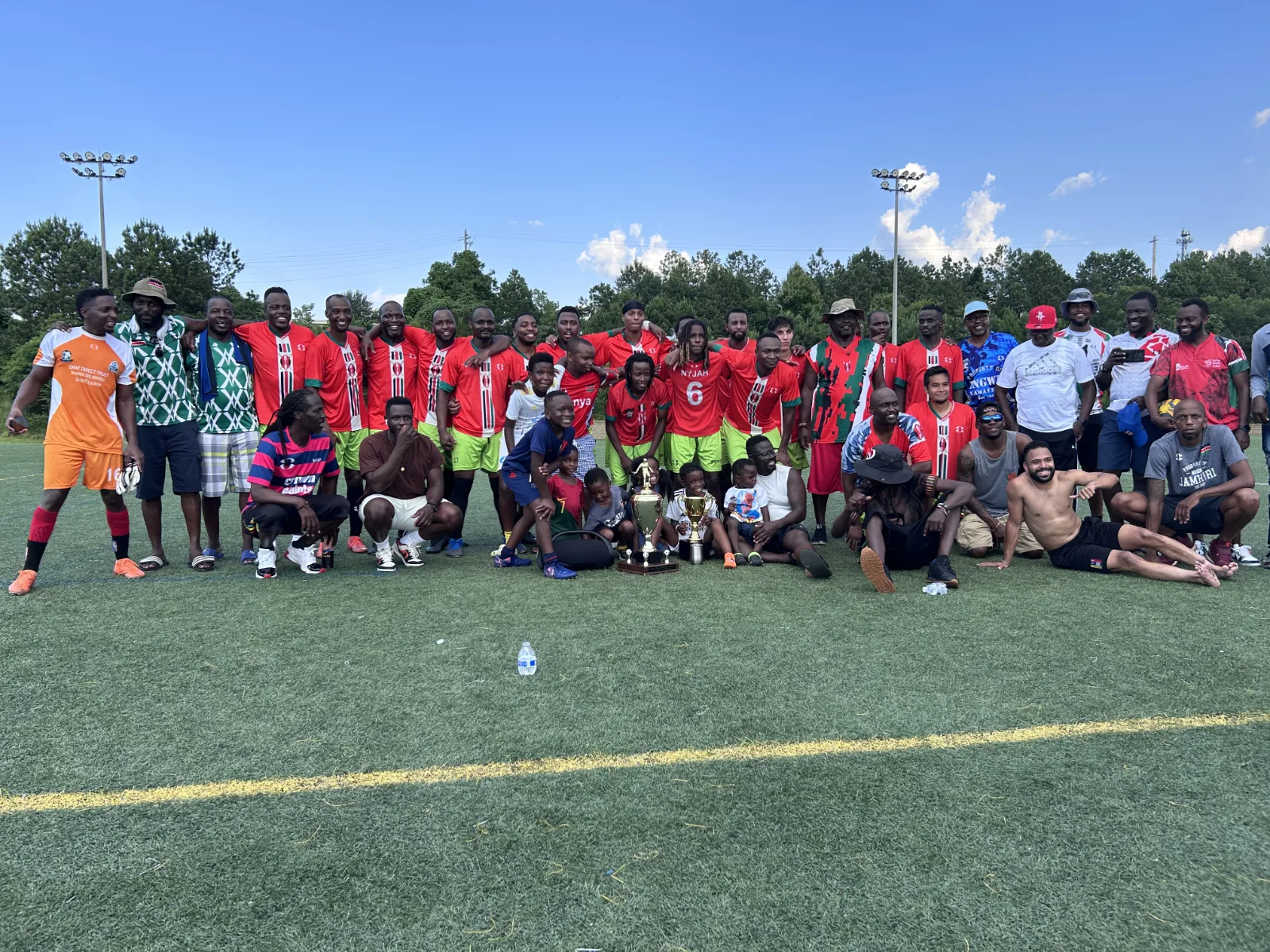 The full Jamhuri FC squad, supporters and families gathered on the pitch with the trophies