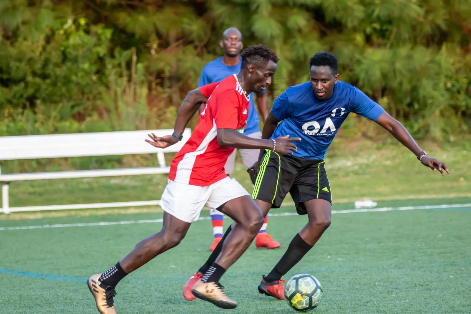 A player in red shielding the ball from a defender in blue